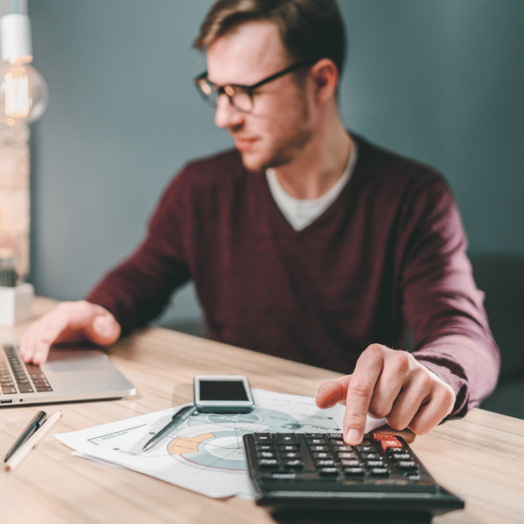 a man sitting on his office desk looking on the laptop and typing on the calculator